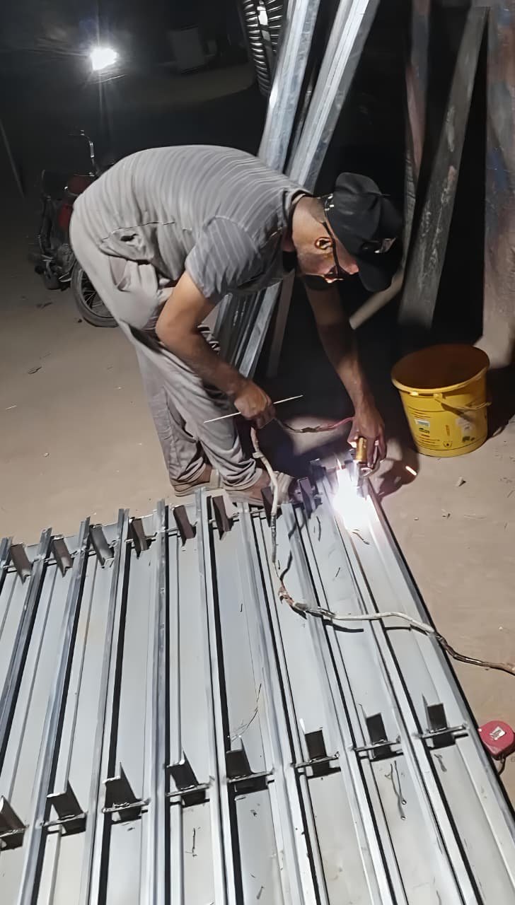 A skilled metal worker welding steel sections in a fabrication workshop while manufacturing a custom iron door or window frame